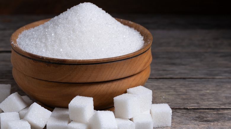 granulated sugar in a wooden bowl with sugar cubes on the side