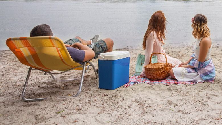 People sitting by a lake with a cooler