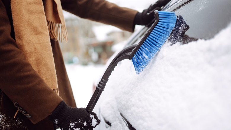 Person using brush to remove snow from a car