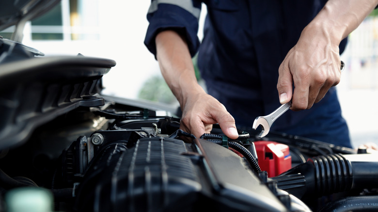 Two hands, one holding a wrench, above a plastic engine cover.