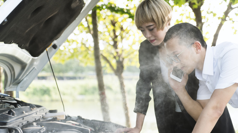 A man and a woman standing in front of a smoking car engine