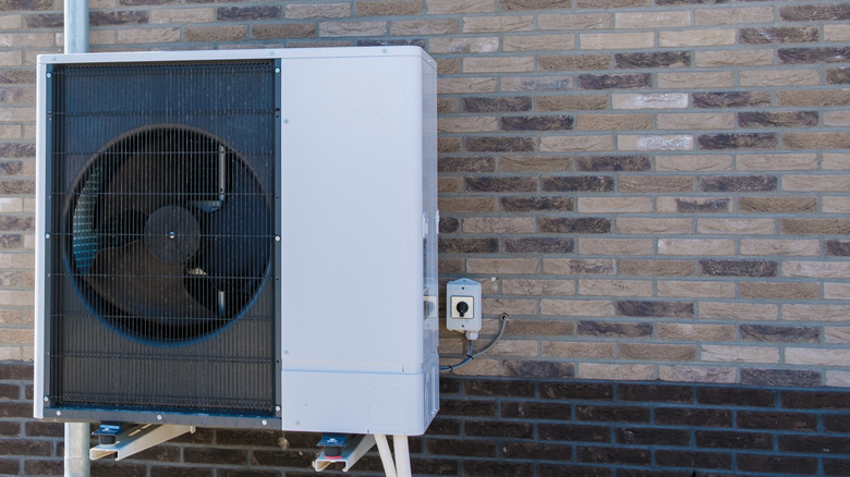 An air source heat pump is mounted on a brick wall