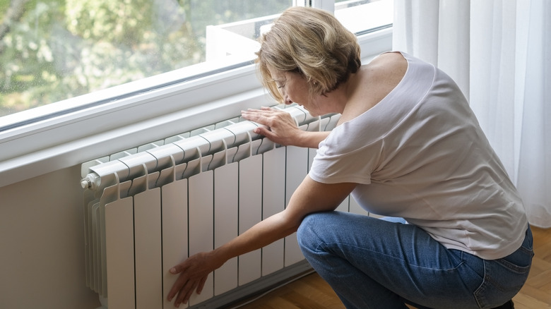 A person kneeling down touching a home radiator.