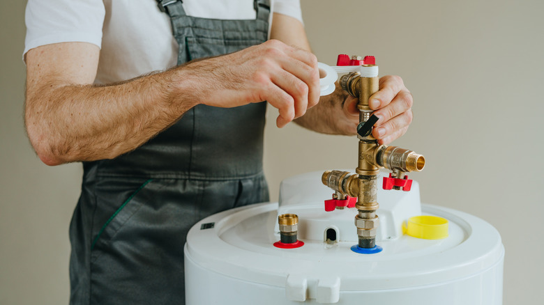 Worker in overalls wrapping plumbing tape around a fitting on a water heater