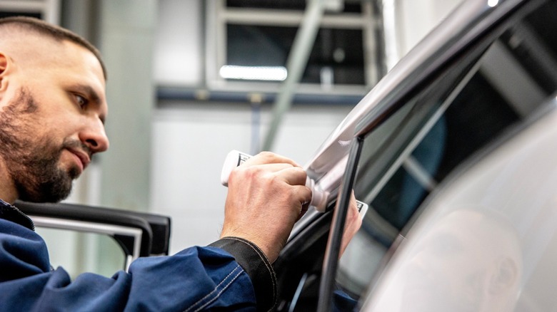 Man applying silicone grease to car door seals before winter