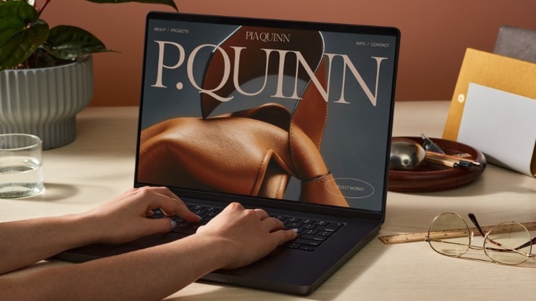 Hands typing on laptop showing P.Quinn website on desk