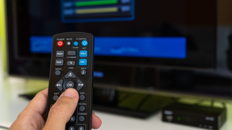 A remote held in front of a TV and connected media boxes