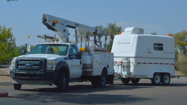 A white Ford heavy-duty truck with a crane attached towing a caravan in a parking lot, front 3/4 view