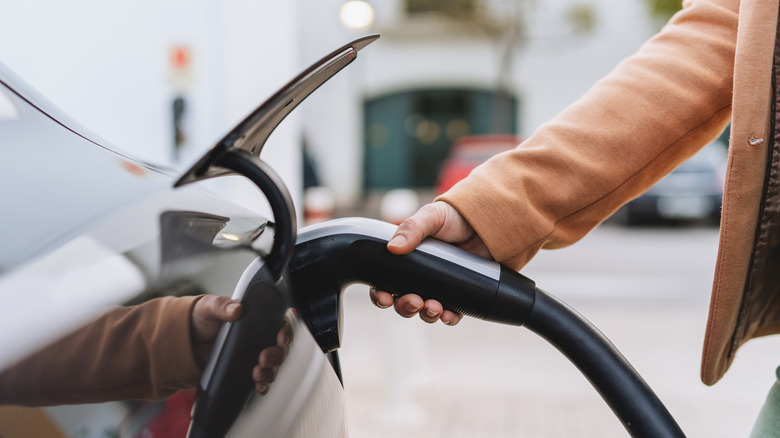 A person plugging charging cable into electric car in outdoor setting