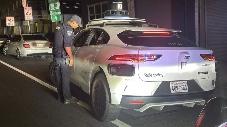 San Bruno PD police officer pulling over a Waymo driverless Jaguar I-Pace, rear 3/4 view