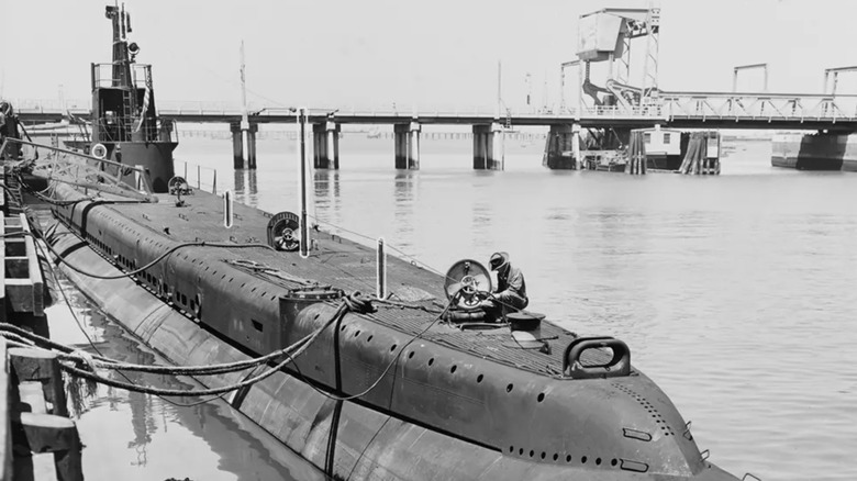Black & white photo of Gato-class submarine moored at a dock with people working on the hull