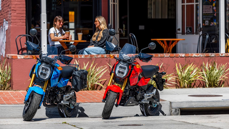 A red and blue pair of Honda Grom motorbikes parked outside a cafe.