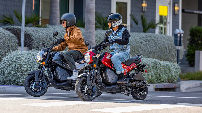 Two riders in helmets riding their Honda Navis through a zebra-crossing on a road