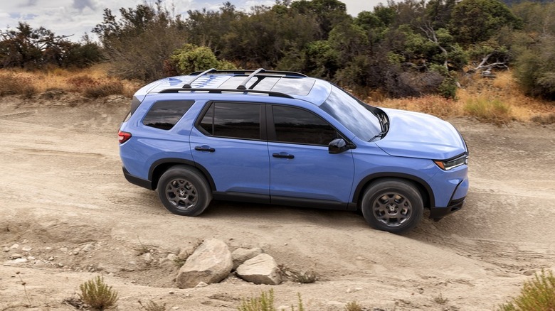 A picture of a blue 2023 Honda Pilot driving on an unpaved road.
