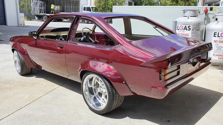 A partially restored classic car in metallic maroon paint