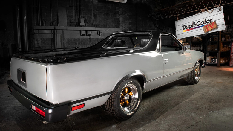 A restored silver Chevrolet El Camino parked in a dimly lit garage with a "Dupli-Color TV" sign hanging in the background.