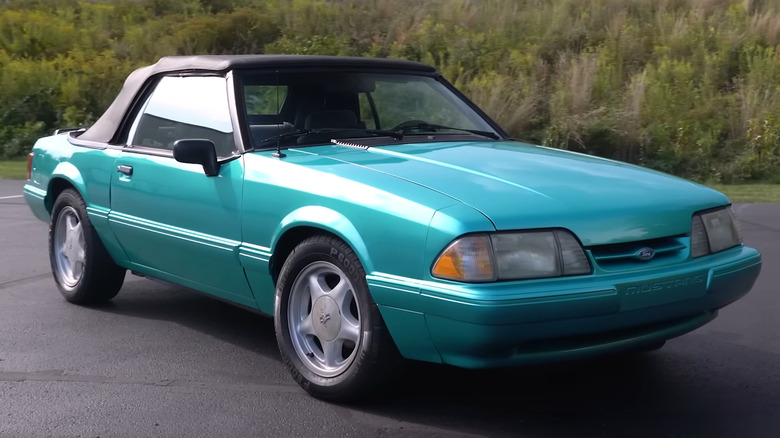A teal 1990s Ford Mustang convertible parked on asphalt with the top up.