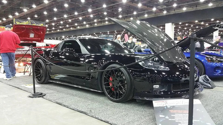 A sleek black Chevrolet Corvette with its hood open on display at an indoor car show.