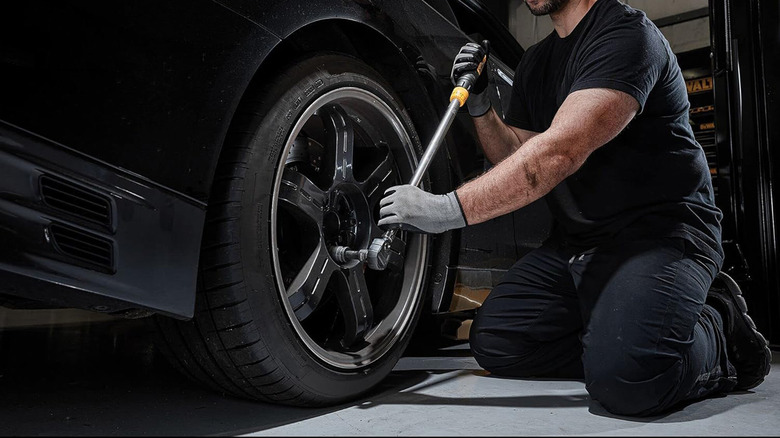 A man using a torque wrench to loosen lug nuts on a wheel