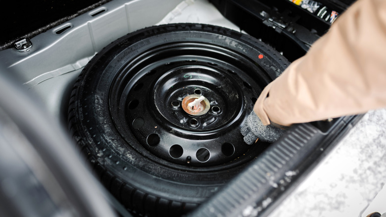 A person grabbing the donut spare tire from the wheel well of a car