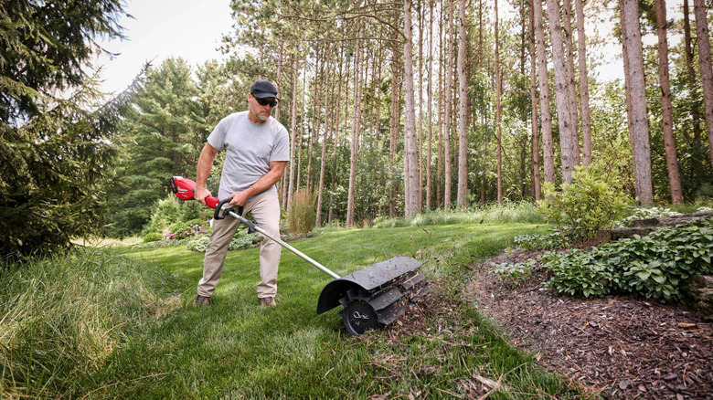 A man edging a lawn along a mulch bed using a Quik-Lok Rubber Broom attachment.