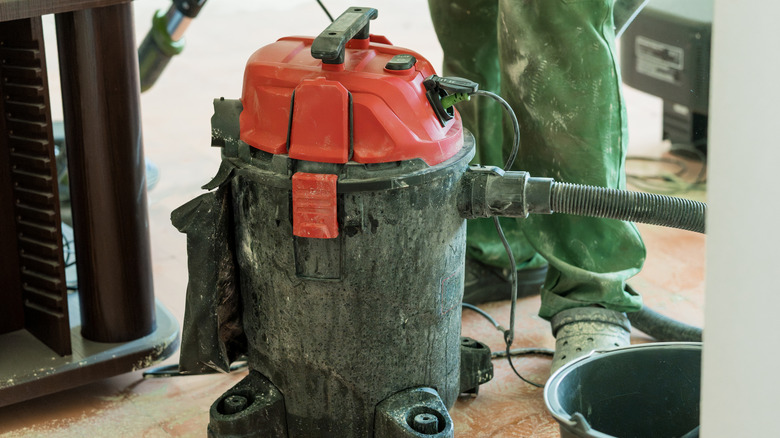 A well-used red shop vacuum stands on a concrete floor during building or remodeling,