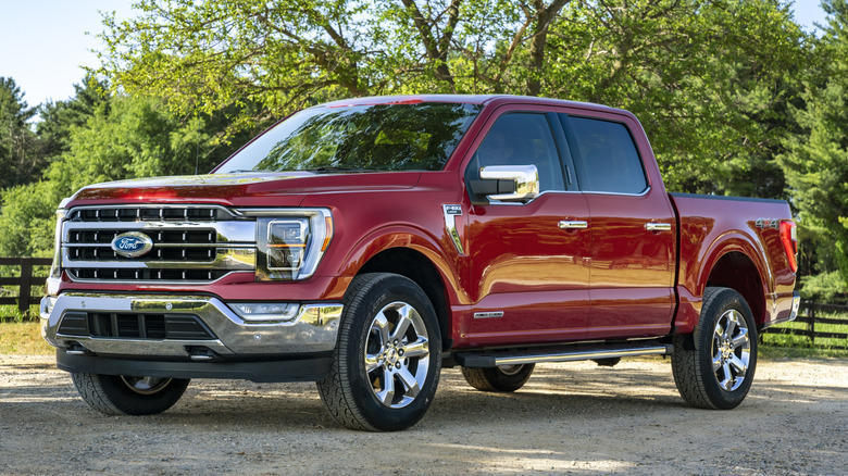 Red Ford F-150 parked on gravel with a tree in background