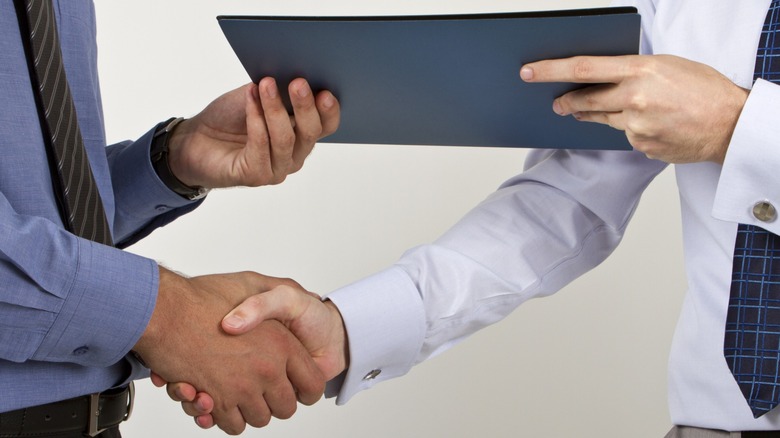 Two men shaking hands and exchanging a folder