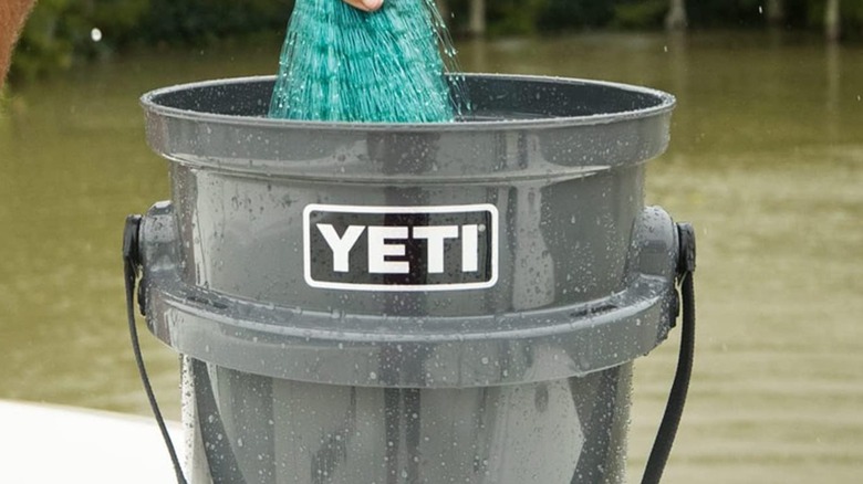 A person pulling a fishing net out of a Yeti bucket.
