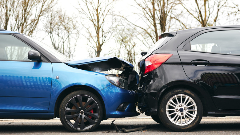 A blue car with a damaged hood that has hit the back of a black car