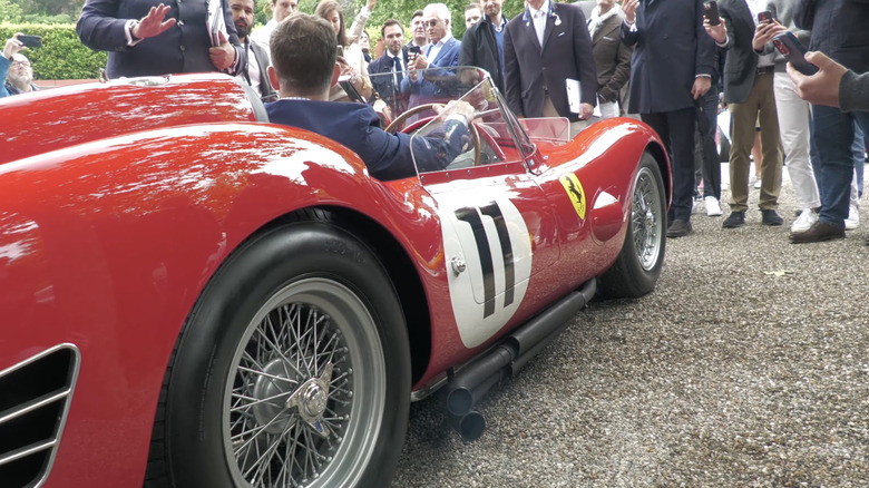 A red Ferrari 250 TR59/60 showcasing its side exhausts to a crowd.