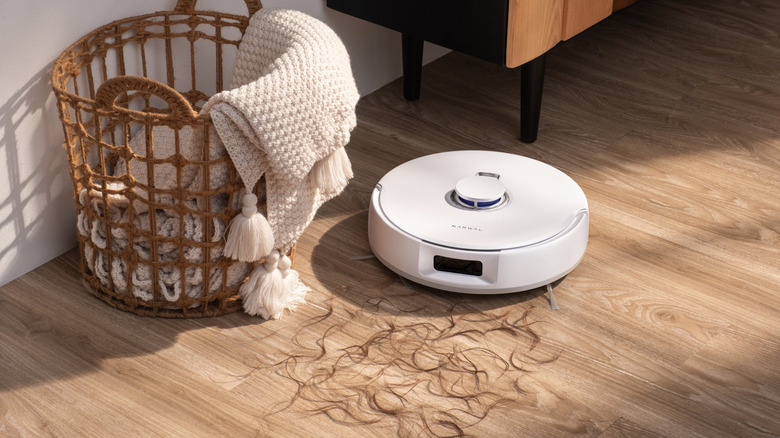 White Narwal Freo Z10 vacuuming strands of hair on a hardwood floor next to a basket with a blanket inside