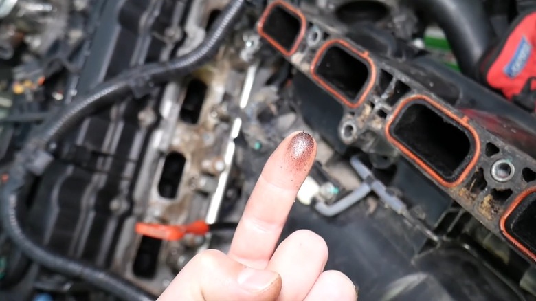A person showing oil on their finger from the intake manifold (seen in back right of pic)