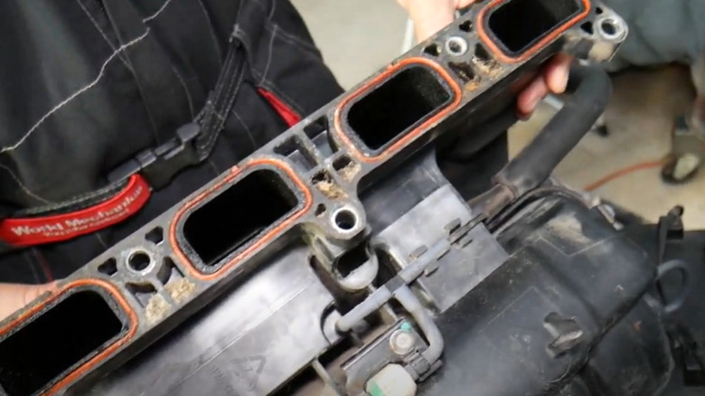 A person holding a car intake manifold showing an oil buildup inside