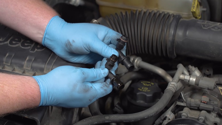 A person holding one new and one old PCV valve during a replacment
