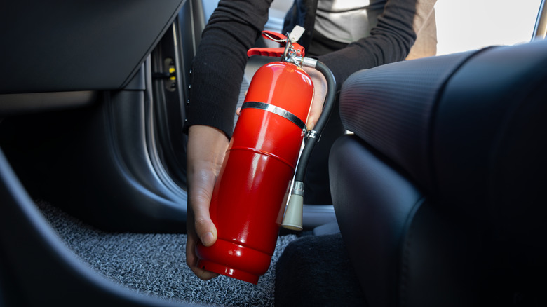 Hands installing a small fire extinguisher inside a car.