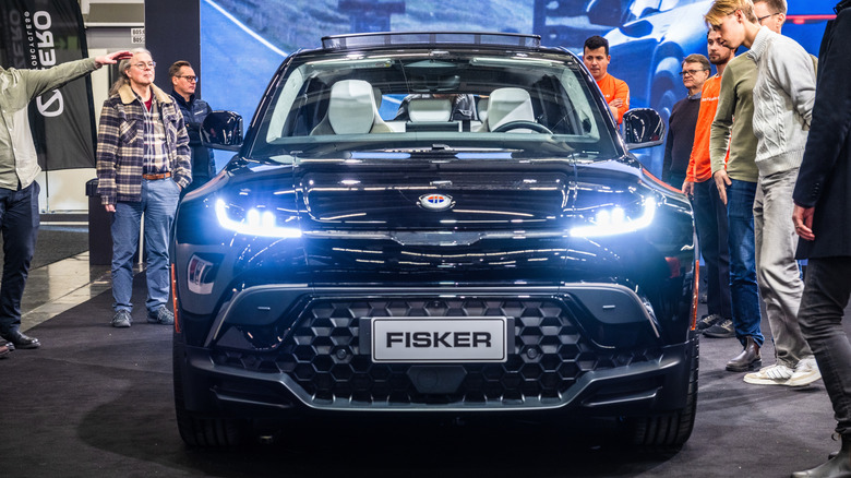 A front-end shot of a black Fisker Ocean SUV parked on display with people around it.