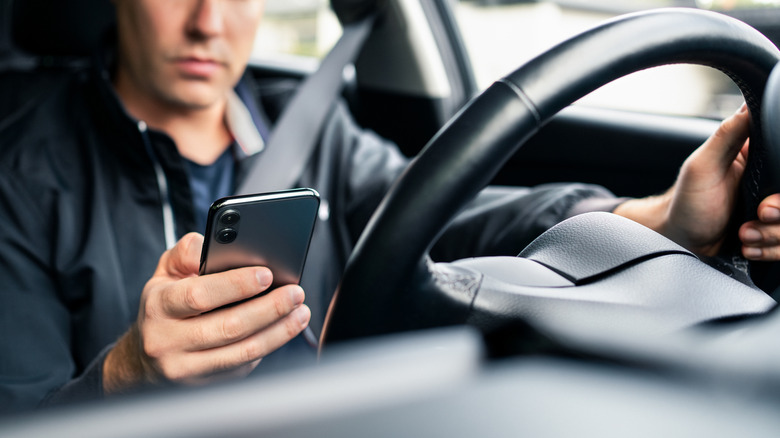 A person gripping the steering wheel with one hand while using the other to hold a phone.