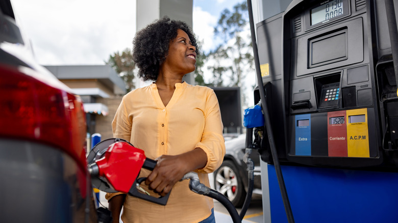 A smiling African American woman filling up her vehicle with a red gas pump