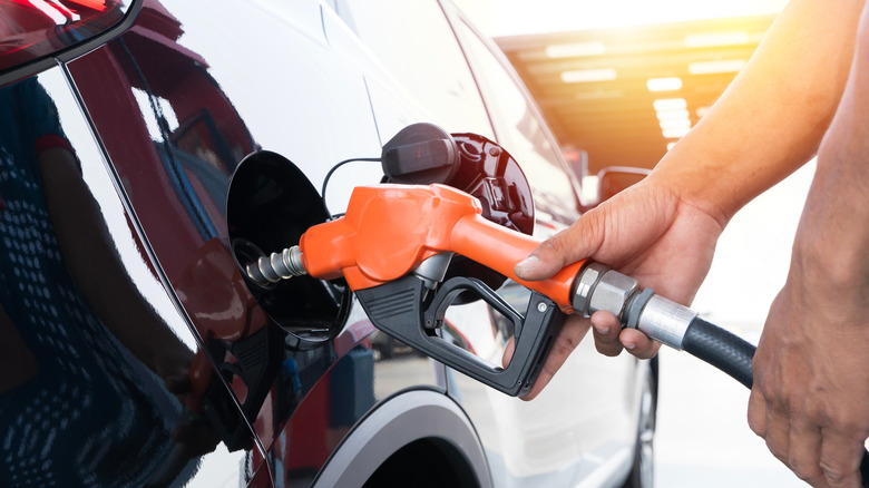 A man holding holding an orane gas pump while filling up a black vehicle