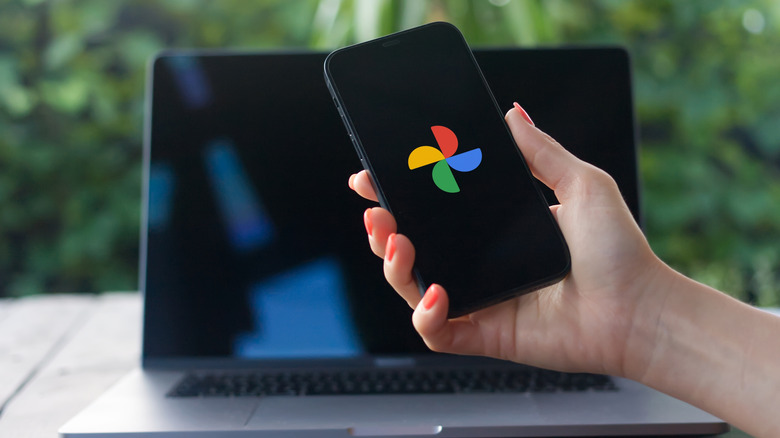 Hand holding a phone with Google Photos logo in front of laptop