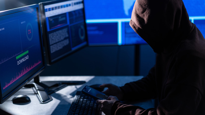 Hooded hacker sitting before banks of computer screens