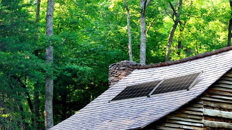 Solar panels on sloped roof of a log cabin in the woods