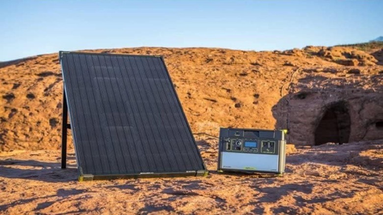 Rectangular solar panel on stand in desert with rocky cave behind it and battery next to it