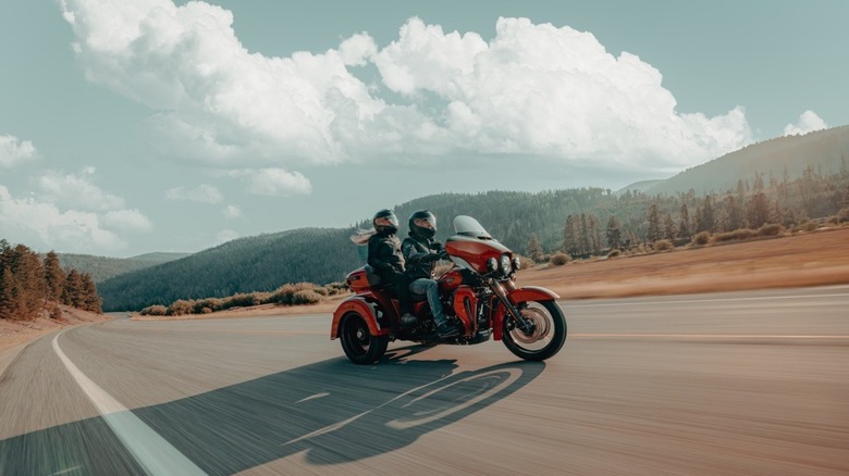 A male and female rider going down an open country road on an orange Harley-Davidson Tri Glide Ultra.