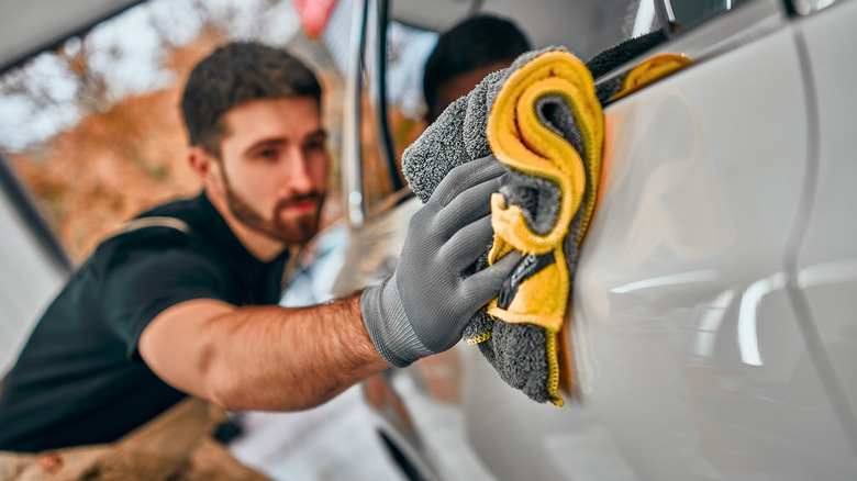 man cleaning white car with microfiber towel