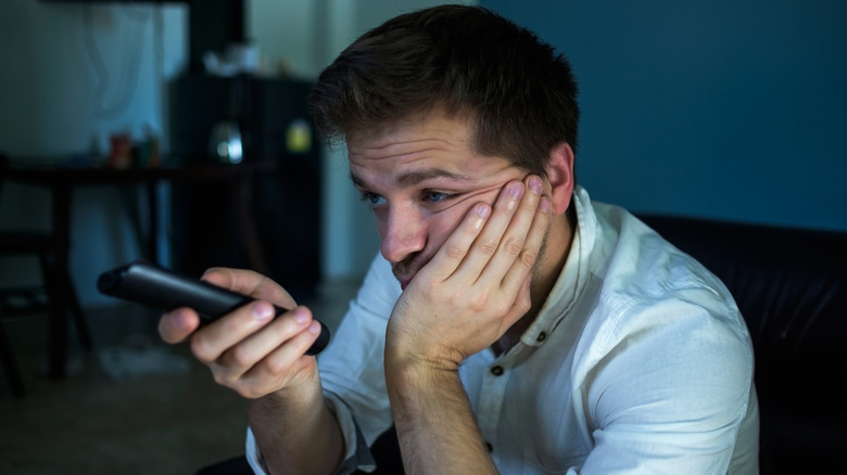 Frustrated man pointing remote control at a TV
