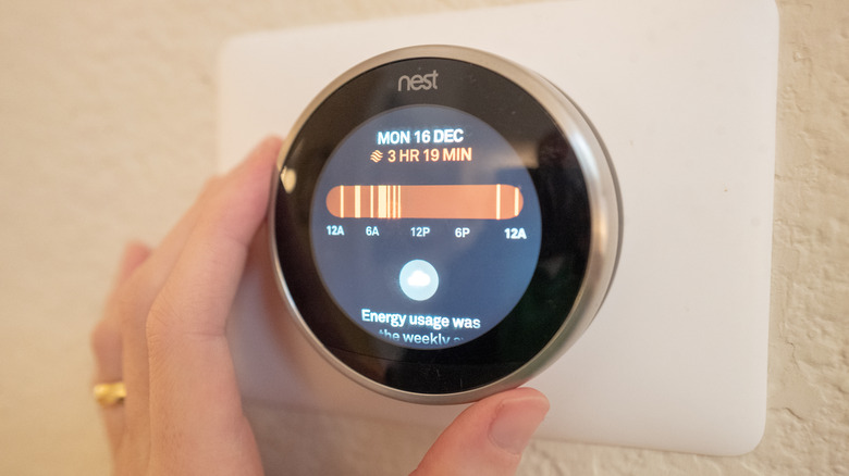 A close-up of a hand adjusting a smart Nest theromostat