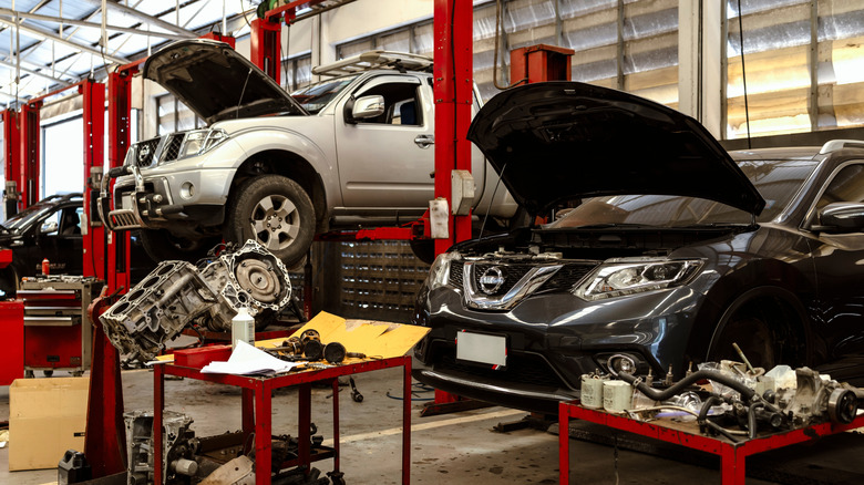 Multiple cars on a lift in a car maintenance shop with scattered car parts around.