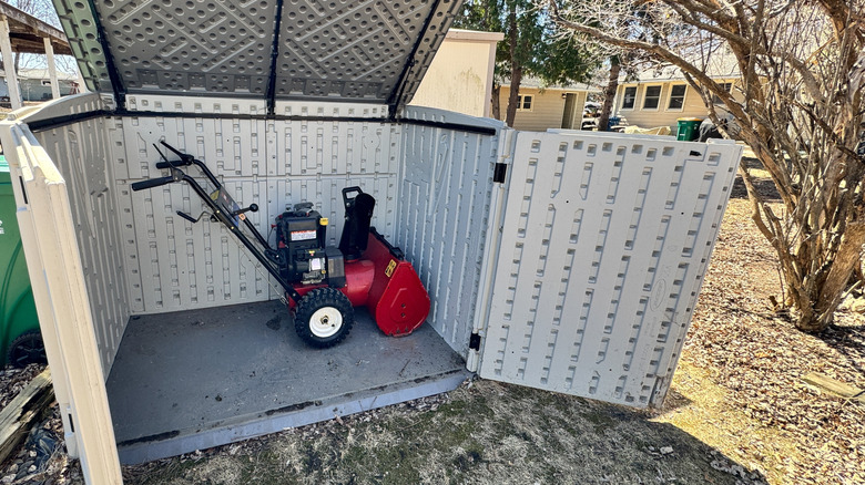 A snow blower stored inside an enclosed outdoor storage container